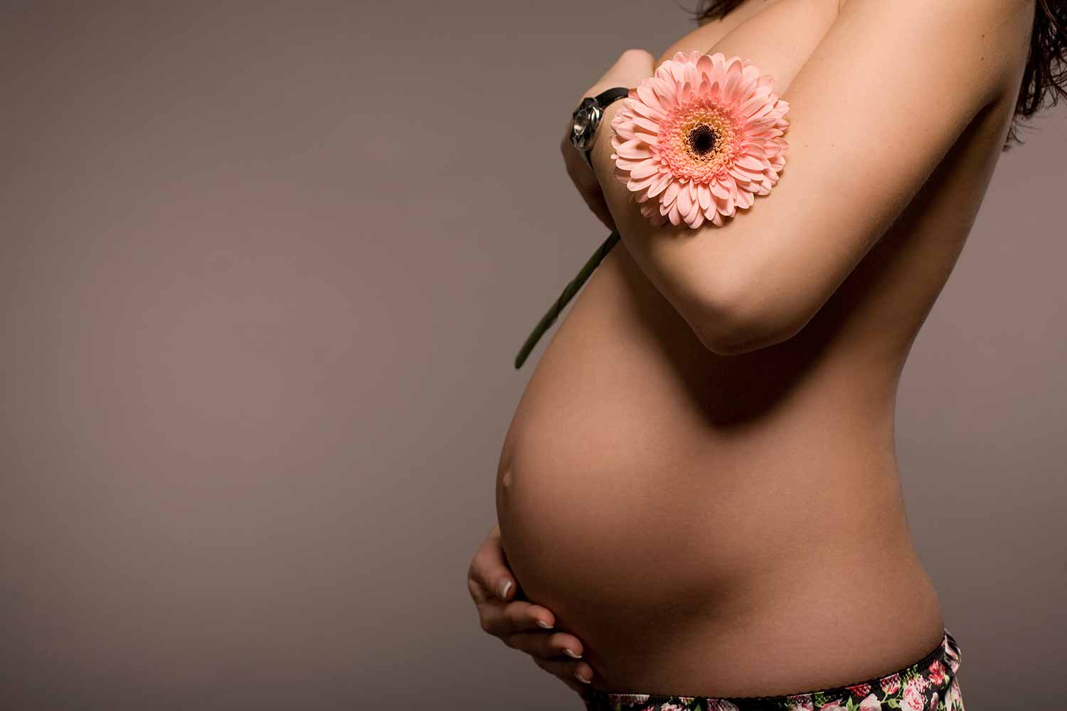 semi clothed pregnant woman holding a flower